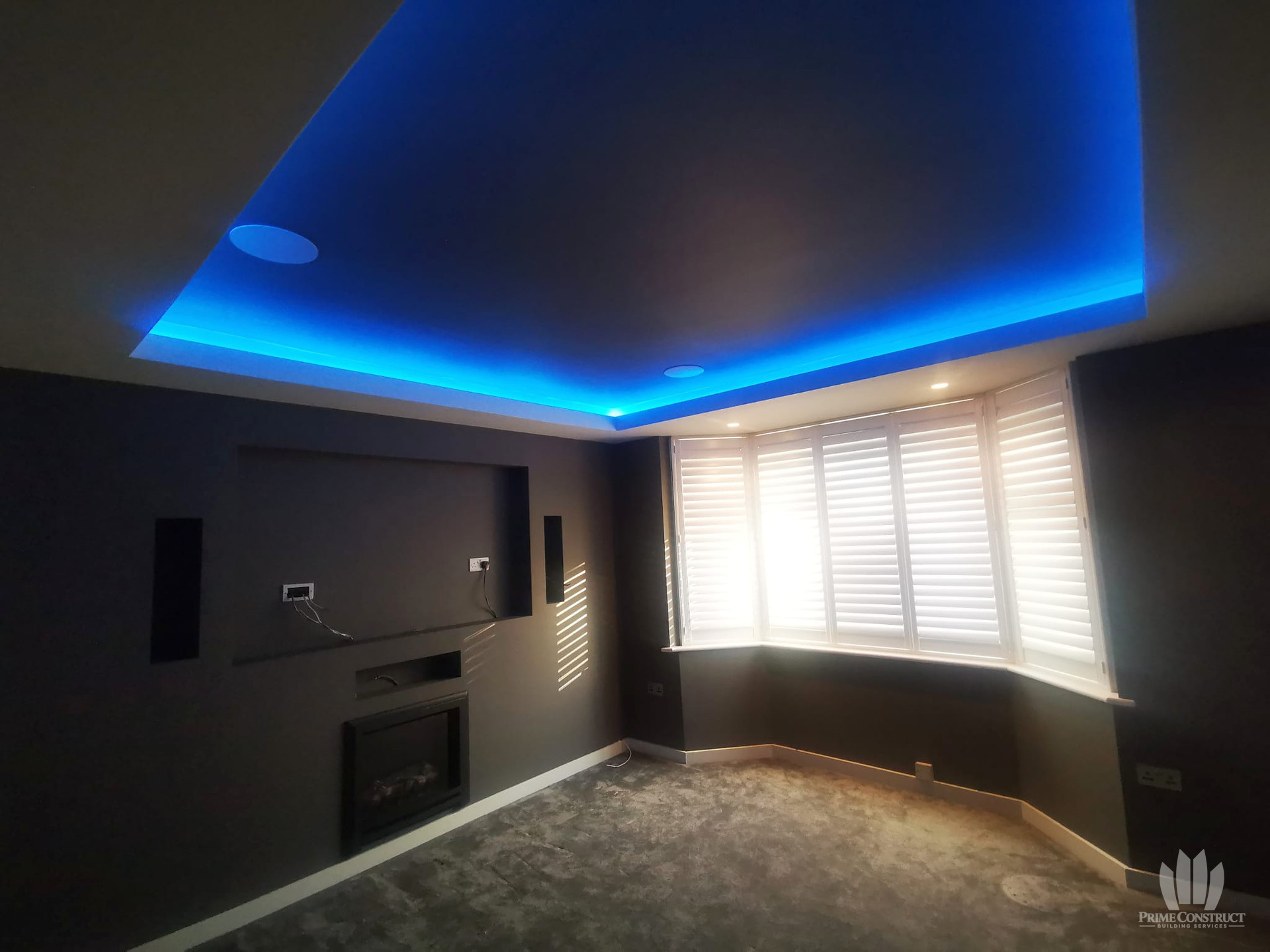 Blue ceiling lighting above the cinema-room feature wall, fireplace and shuttered bay window.