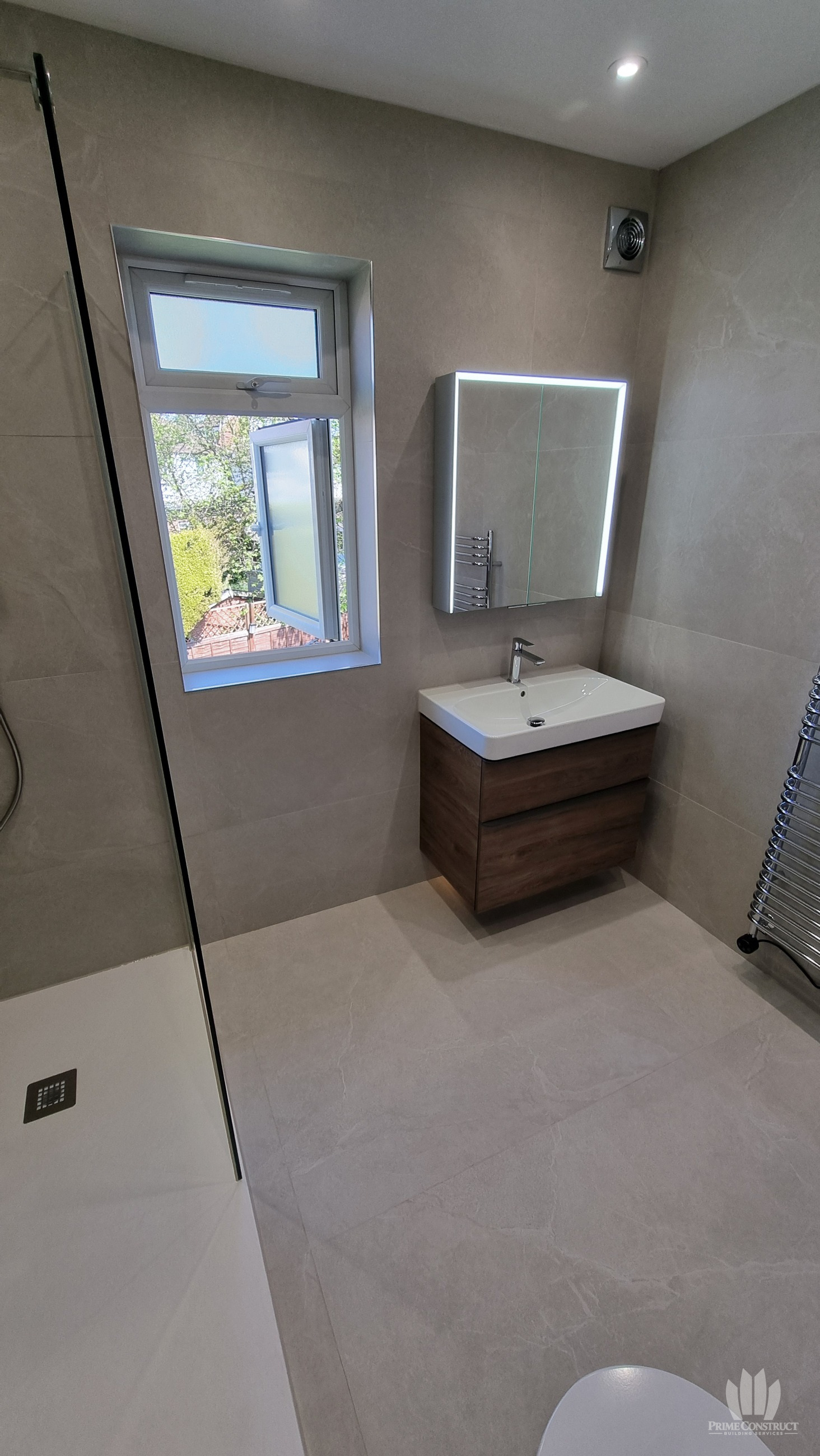 Finished window and illuminated mirror above wall-hung vanity, with shower at left