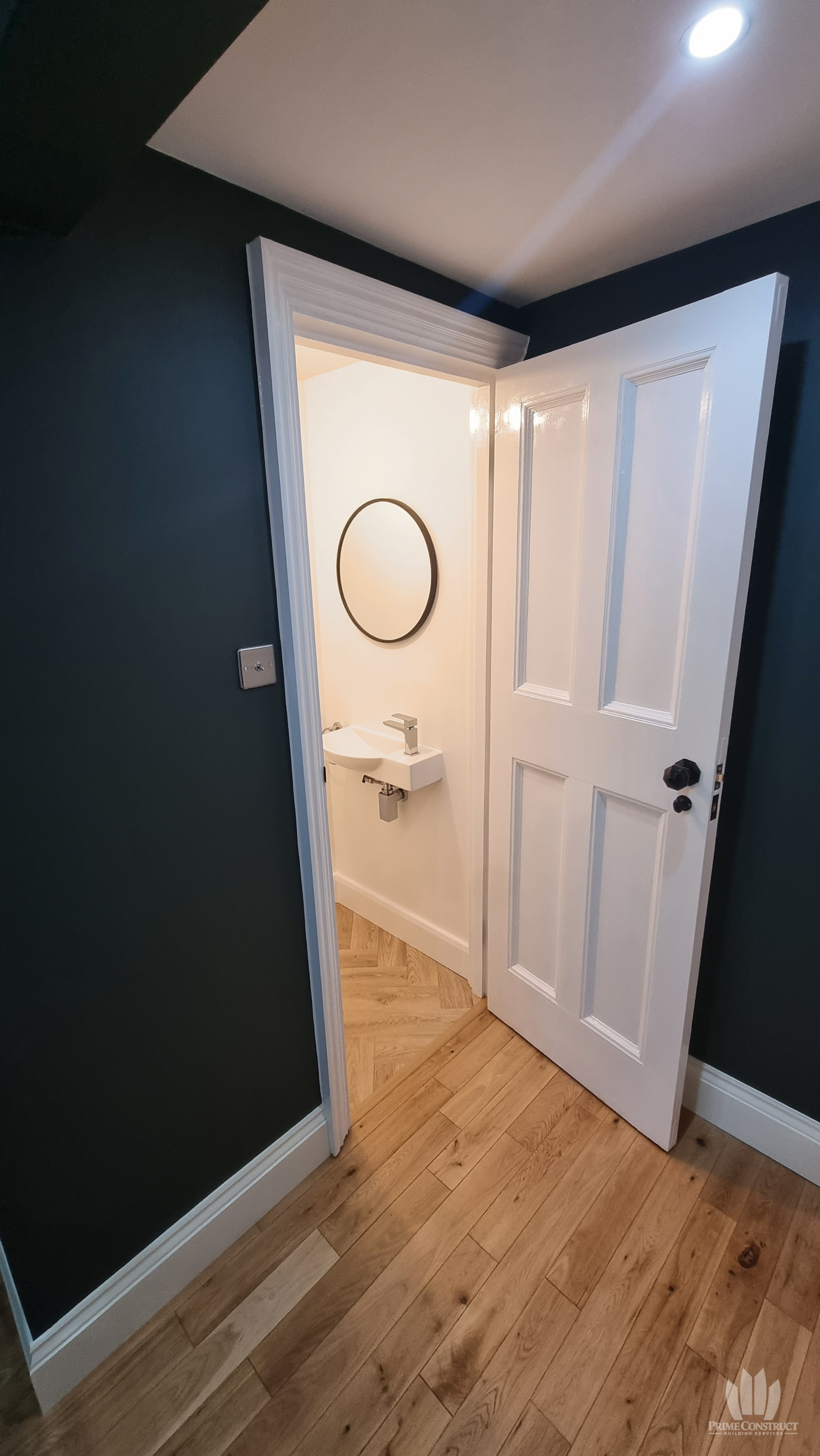 Open cloakroom doorway with compact basin and round mirror