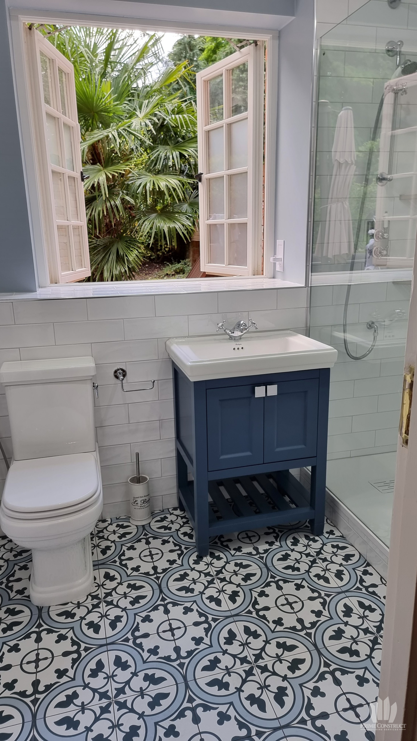 Blue vanity, traditional-style WC, patterned floor and glass shower