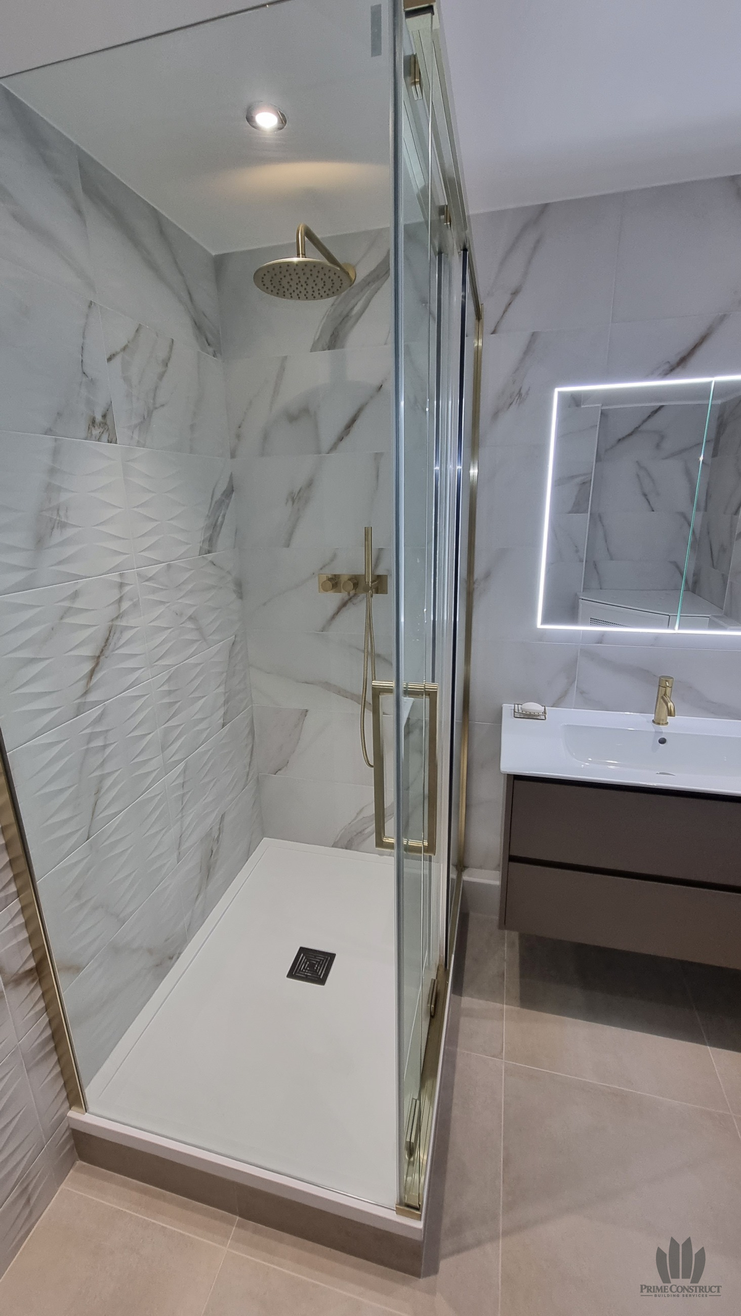 Finished raised shower and adjacent floating vanity with illuminated mirror. Strong portrait hero candidate showing the plinth, texture and fittings.