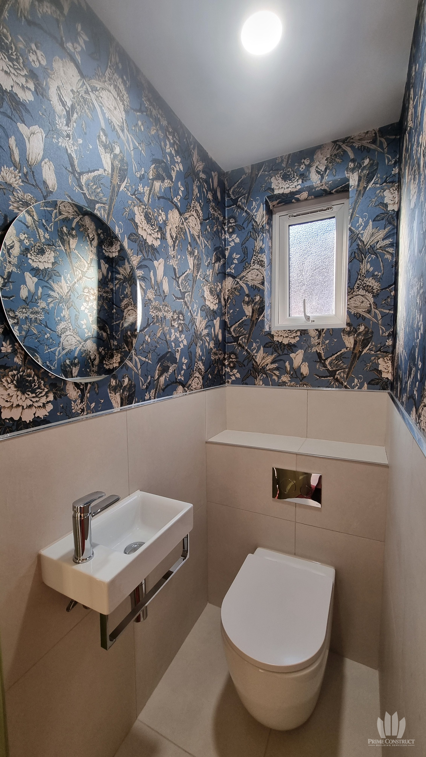 Compact cloakroom with botanical wallpaper, oval mirror, small basin and concealed WC.