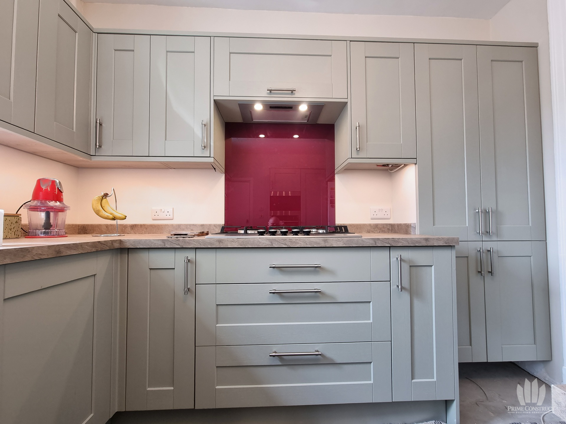 Magenta splashback fitted behind gas hob in grey kitchen.