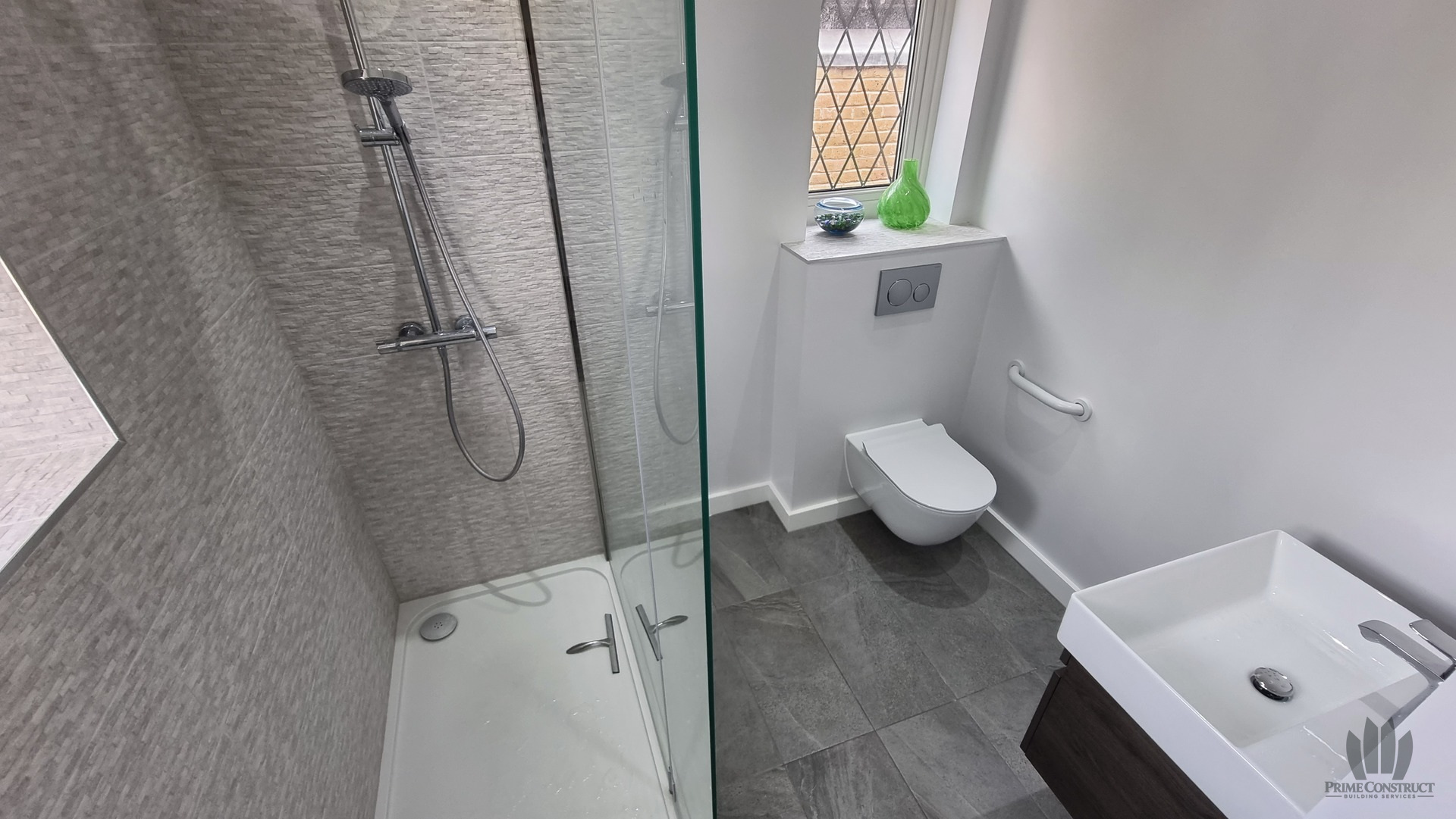 Finished shower-room views showing long tray, glass enclosure, rainfall shower and grey textured tiles.